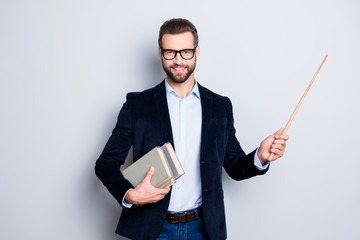 Portrait of cheerful teacher with stubble in shirt jacket, having books in hand and showing with pointer on empty place, copy space, looking at camera, isolated on grey background