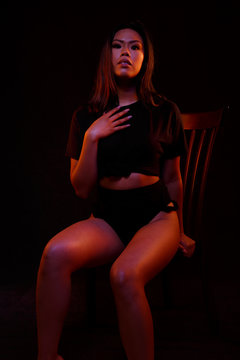 Fit young asian woman in black one piece poses on a chair under colored lights