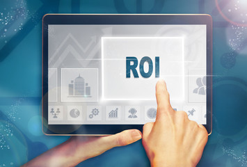 A hand selecting a Return on Investment business concept on a computer tablet screen with a colorful background.