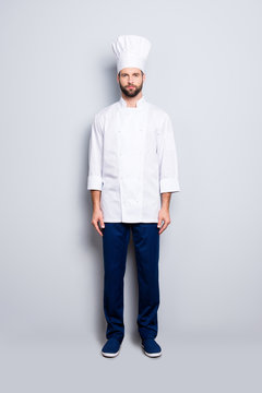 Full size fullbody portrait of attractive stylish chef cook with stubble in beret, looking at camera, isolated over grey background
