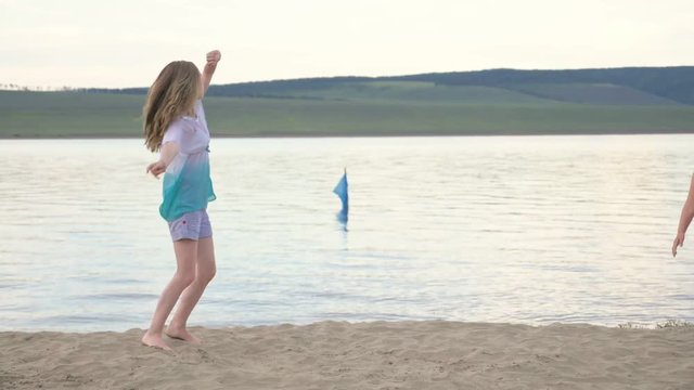 Two happy child on beach play games. Children perform acrobatic stunts tricks. They have fun and jump dancing. Their hair fluttering in the wind.