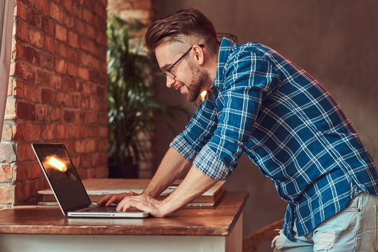 Handsome Student In A Flannel Shirt Working On A Laptop Computer In A Room With A Loft Interior.