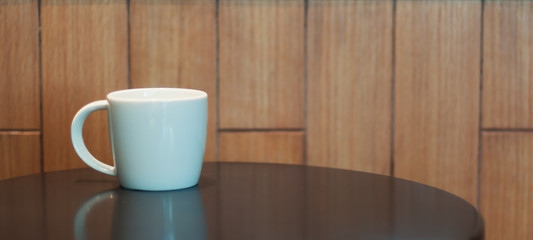 White middle coffee cup lay on black table and wooden wall.