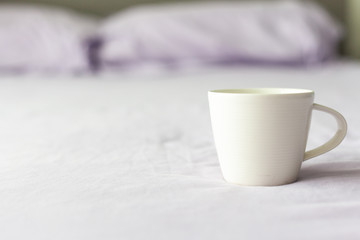 White coffee cup on the bed in morning.