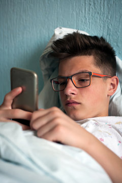 young teenager lying in bed and using smartphone