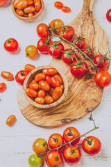Fresh cherry tomatoes on olive wooden bowls and board, white background, top view