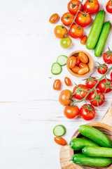 Fresh tomatoes cherry and cucumber in olive wooden bowls and board, white background