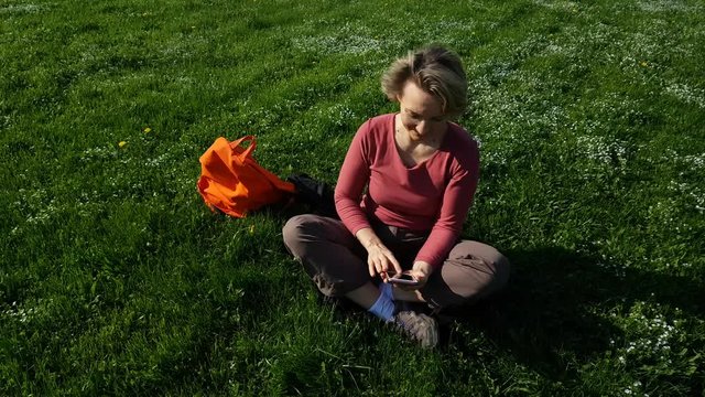 Adult Woman sitting on green grass with mobile phone
