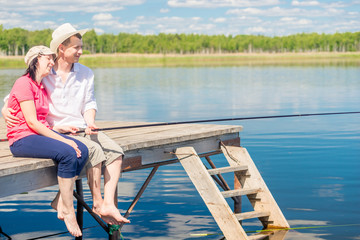 Fototapeta premium A married couple on a pier with bare feet catching a fish on a beautiful lake