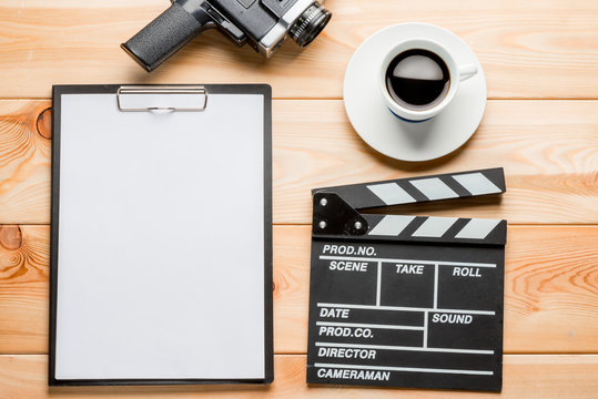 notebook for writing a script, clapper, retro video camera and coffee cup on a wooden background top view