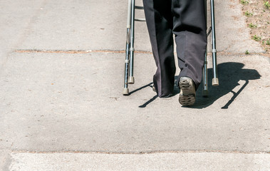 Old disabled woman walking alone and depressed on the street in the city helped by adjustable walker stick or cane