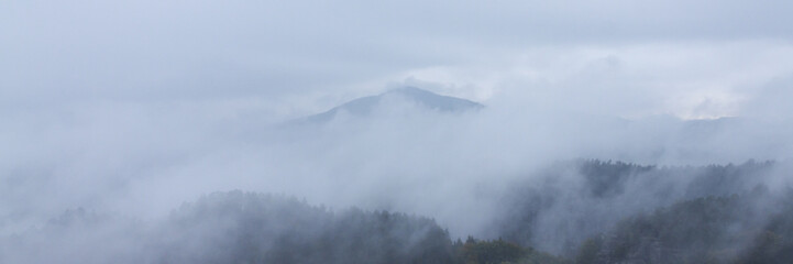 Panoramic view on peaks of mountains surrounded by clouds and fog