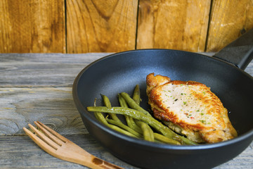 fried chicken fillet and asparagus in a frying pan on an old wooden background