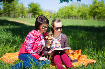 Mom and daughter teenager resting on a meadow in the grass and reading a book