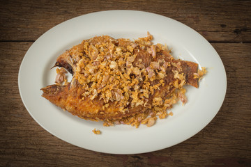 asia-asian food. thai food. fried nile tilapia river fish with garlic. on dish ceramic. on old wood background