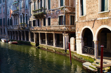 Fototapeta na wymiar Afternoon sunlight illuminates a portico beside a Venetian canal