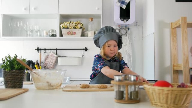 Preschool girl baker puts biscuits on a baking sheet