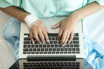 Fototapeta na wymiar Patient using laptop in bed. Typing action. Young attractive chinese woman in hospital bed. Connected world and mobile office concept.