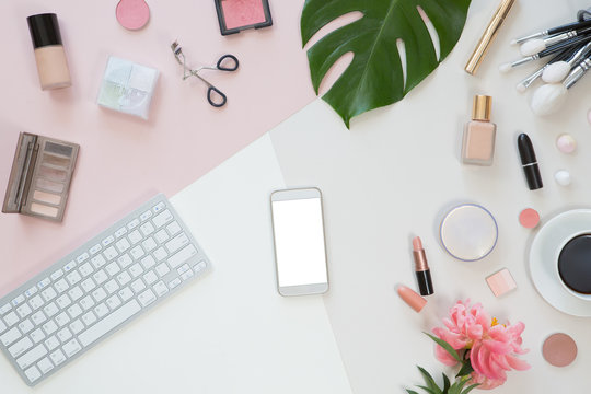 Top view of office desk with laptop, mobile phone, green leaves, flowers and coffee. Flat lay. Home office or beauty blogger workspace. Women fashion accessories isolated on pink and white background. - Powered by Adobe