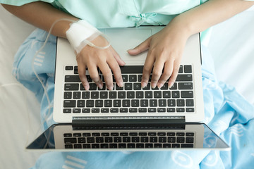 Fototapeta na wymiar Patient using laptop in bed. Typing action. Young attractive chinese woman in hospital bed. Connected world and mobile office concept.