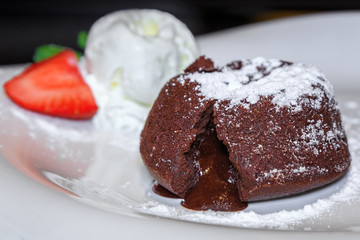 Теплый шоколадный фондант с шариком мороженого и клубникой на белой тарелке.