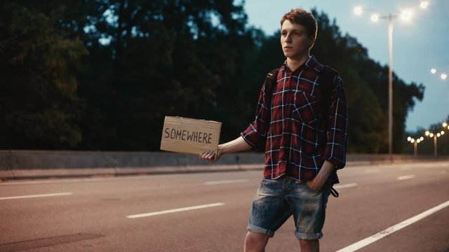 Traveler, young man hitchhiking with sign on the road at night