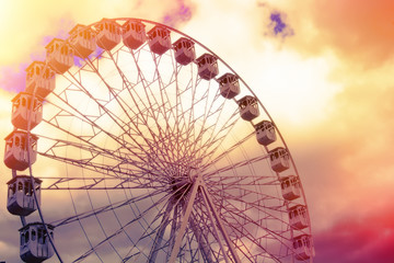 A Ferris wheel at the fair with a beautiful colored cloudy sky.