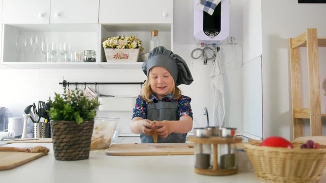 Cheerful little girl in apron rolls out the dough in the kitchen