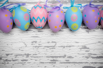 A group of pastel colored Easter eggs on a white, aged wooden background with copy space.