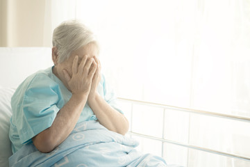 Elderly patient alone in bed. Alone and stress, missing her grand children. Hands on face pose. Very senior, old chinese woman.