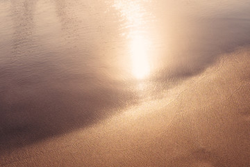 Sunset reflection on calm ocean and golden sand. Warm colored filter effect