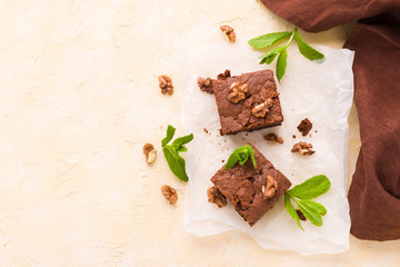 Brownie sweet chocolate dessert with walnuts and meant leaves on white paper with copy space on pastel beige background.