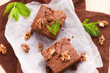 Brownie sweet chocolate dessert with walnuts and meant leaves on white paper with copy space on pastel beige background.