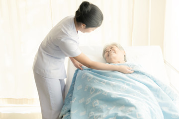 Obraz premium Nurse with patient. Routine health check and putting elderly patient to bed. Female nurse with senior chinese woman.