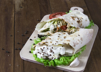 Shaurma chicken roll in a pita with fresh vegetables and cream sauce composition on wooden background