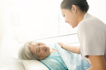 Fototapeta premium Nurse with patient. Routine health check and putting elderly patient to bed. Female nurse with senior chinese woman.