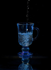 Glass cocktail glass is filled with a trickle of water. Dark background.
