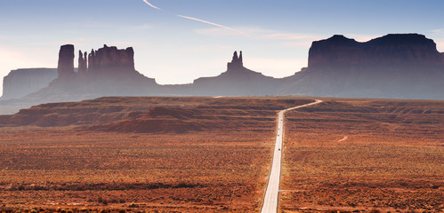 A road in the Utah desert with mountain plateaus, buttes in the background