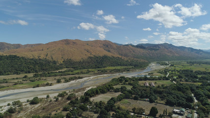 Mountain valley with village, river, farmland in the Philippines, Luzon. Aerial view: Mountain valley with green trees and river.