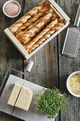 Close-up photo of tasty baked sticks with cheese in box with green plant on wooden table background
