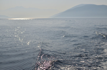 Sea surface with a land in a distance with a morning mist and sunlight twinkles and reflection