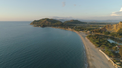 Aerial view of seashore with beach and mountains with sky and clouds at sunset. Philippines, Luzon. View of the ocean with the coastline. Tropical landscape in Asia.