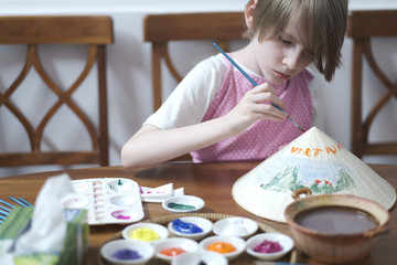 Portrait of a child painting a traditional Vietnamese straw hat with a tassel