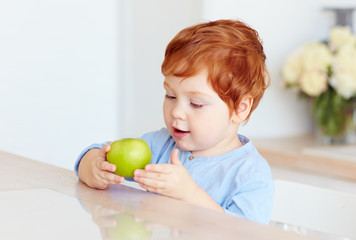 Fototapeta na wymiar cute redhead toddler baby eating tasty green apple