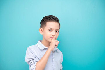 Young boy isolated in blue. Handsome early teenage boy portrait. Happy hush silence pose.