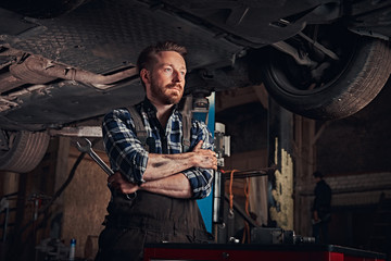 Fototapeta na wymiar Mechanic crossed hands while standing under lifting car in a repair garage.