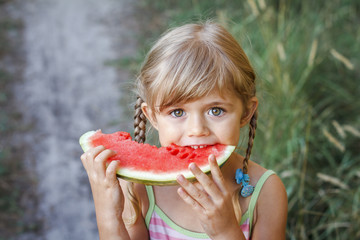 Portrait of cute little girl with pigtails eating yummy watermelon outdoor in hot summer day in vacation. Healthy eating. Vegetarian. Immunity	