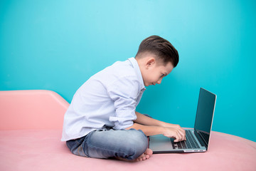 Young software programmer isolated in blue. Handsome early teenage boy portrait. Playing with notebook. Technology concept.