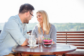 Happy young couple drinking coffee and talking while relaxing in a riverside cafe. Romantic vacation moments