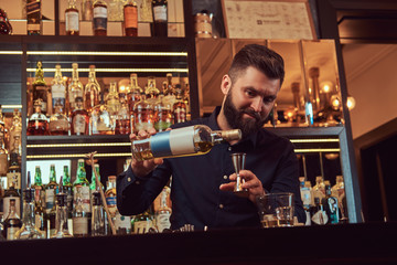 Stylish brutal barman in a black shirt makes a cocktail at bar counter background.